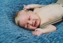 Un bambino di 2 mesi è sdraiato con pantaloni lavorati a maglia su una coperta grigia, abbigliamento per neonati.