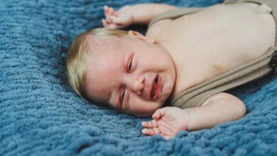 Un bambino di 2 mesi è sdraiato con pantaloni lavorati a maglia su una coperta grigia, abbigliamento per neonati.