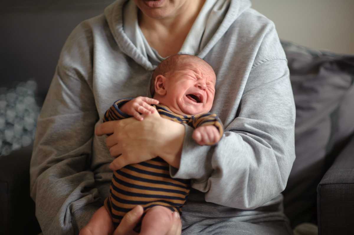 Un bambino di 2 mesi è sdraiato con pantaloni lavorati a maglia su una coperta grigia, abbigliamento per neonati.