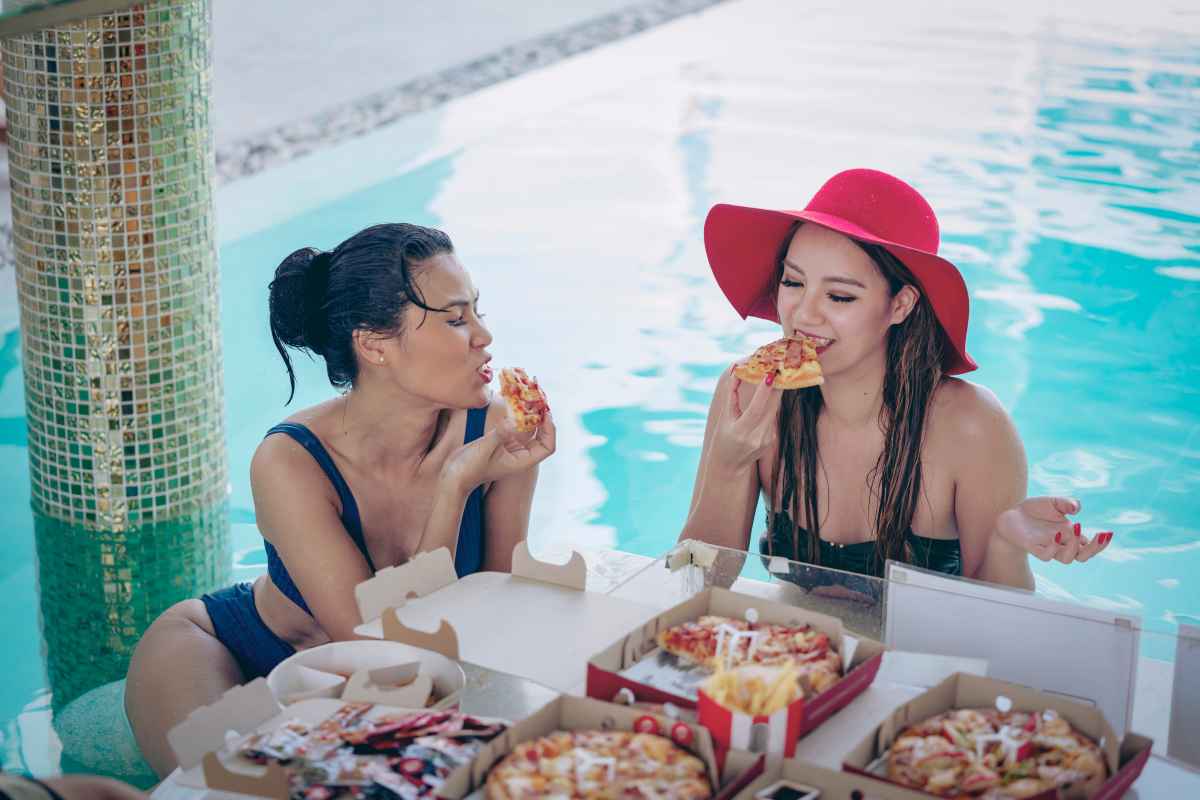 Due ragazze che mangiano pizza si rilassano meglio in piscina