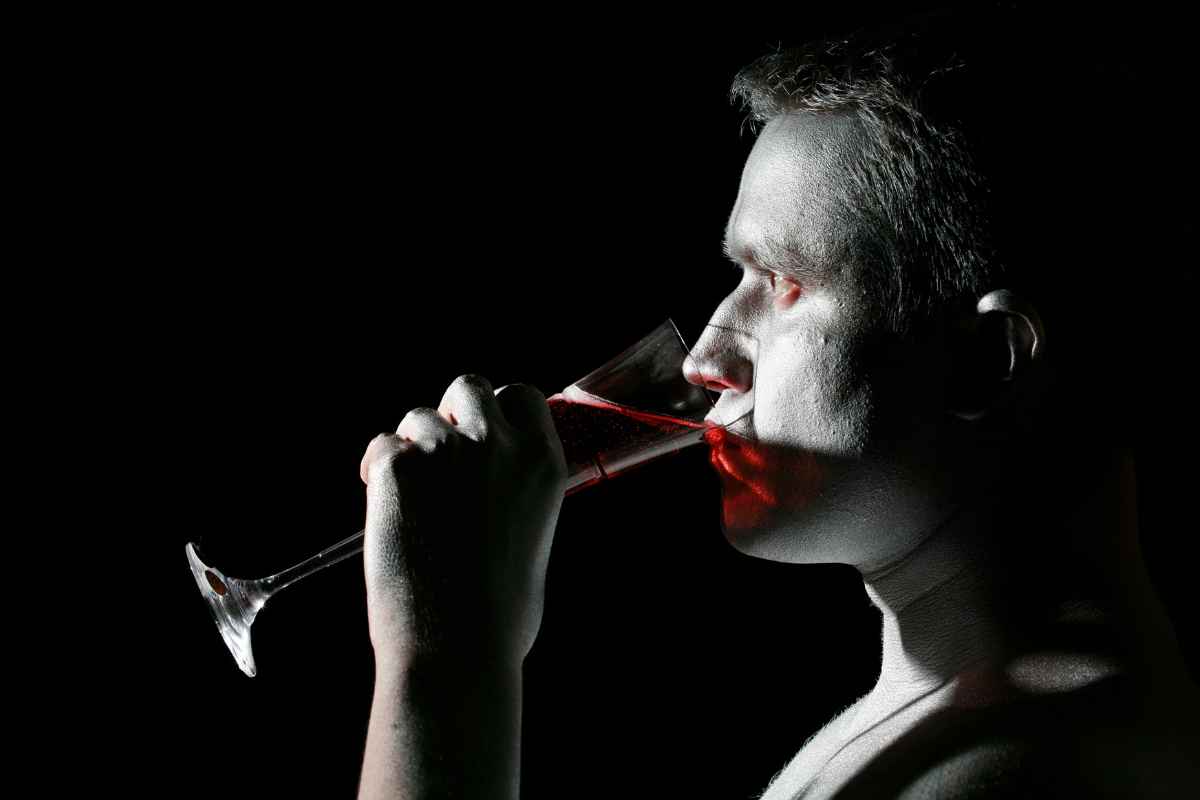un uomo travestito da vampiro finge di bere del sangue da un bicchiere