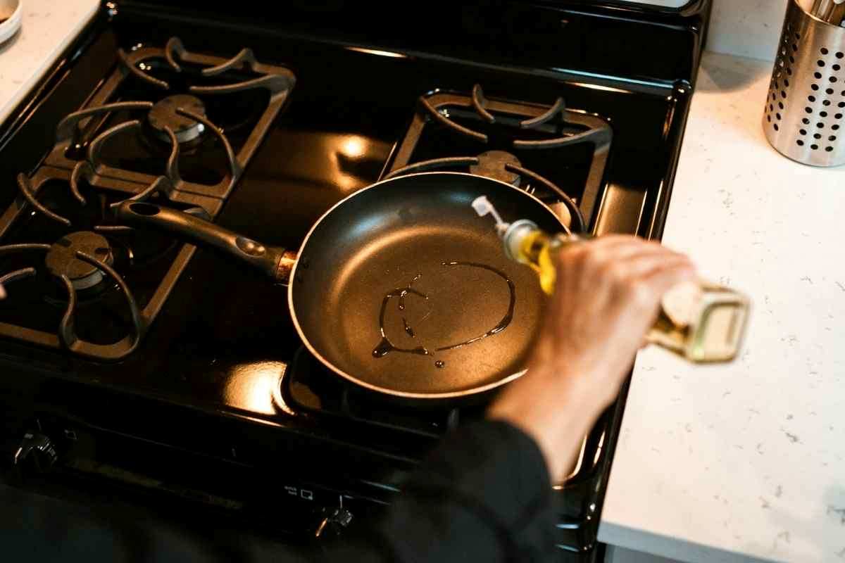 una persona versa l'olio in una padella