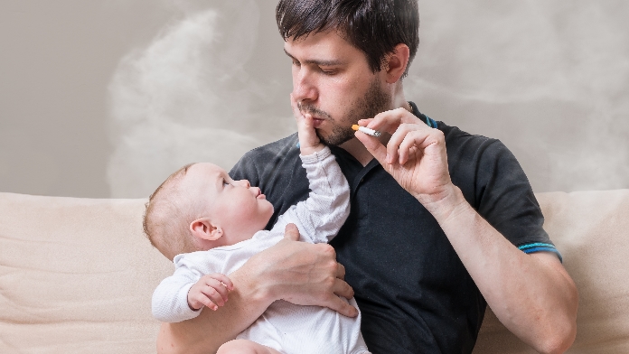 Un papà fuma con in braccio il suo bambino