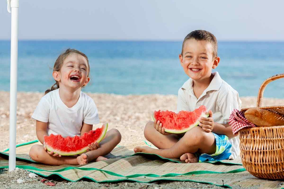 due bambini mangiano una fetta di anguria in spiaggia