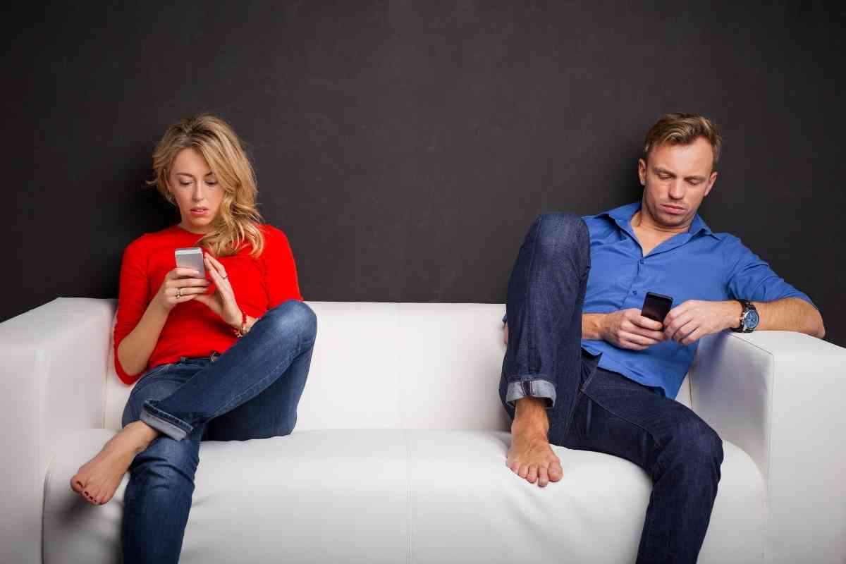 una coppia è seduta su un divano concentrata sui loro cellulari