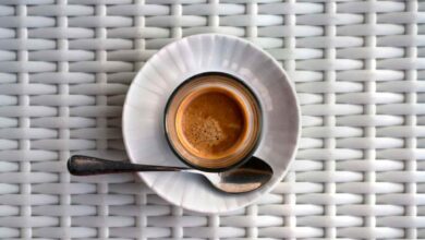 Espresso aromatico caldo con schiuma. Una bevanda preparata al momento servita in una tazza moderna su un tavolo di vimini chiaro.