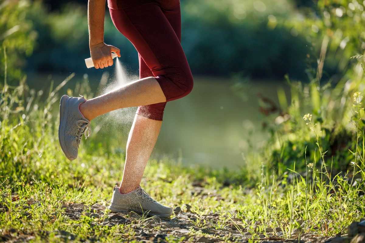 donna in mezzo al prato che spruzza spray repellente per le zecche sulle gambe