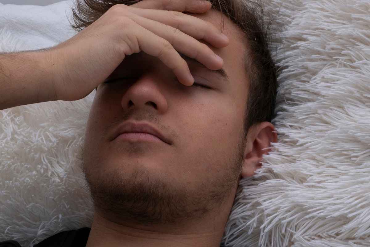 un uomo è sdraiato a letto con il mal di testa e la nausea