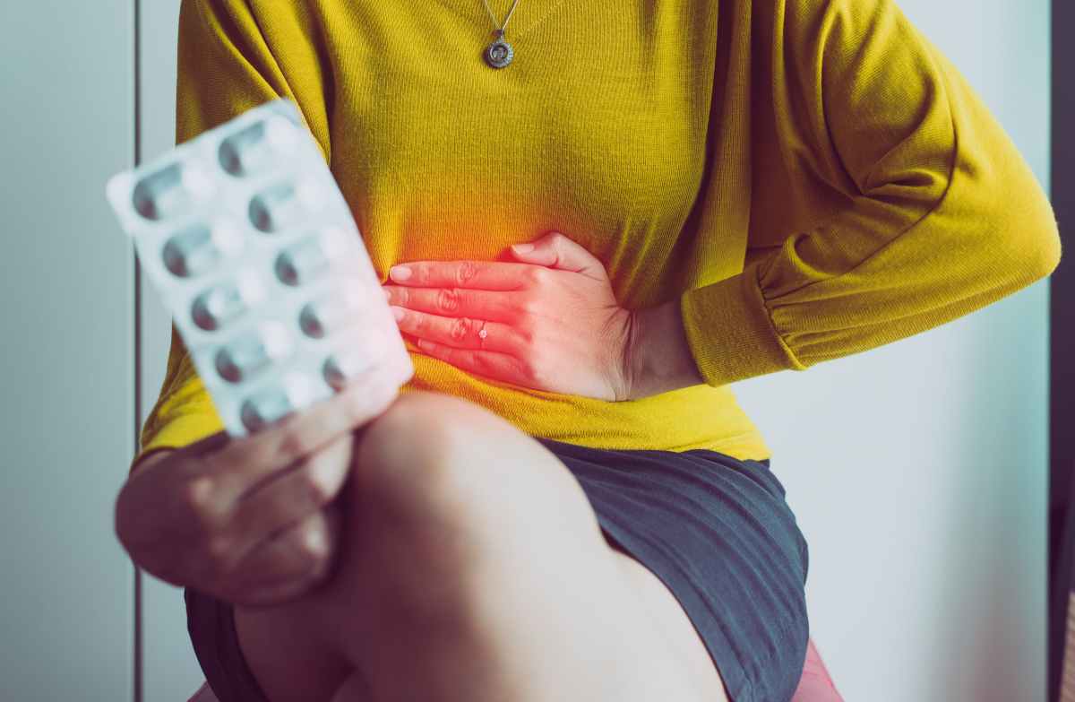 una donna con una mano sul basso ventre e un blister di compresse
