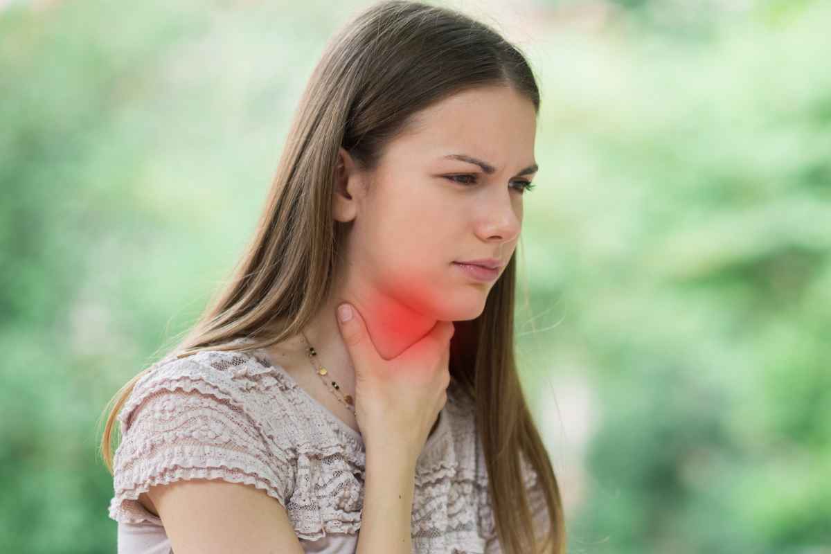 una donna si mette una mano sulla gola per indicare che ha male