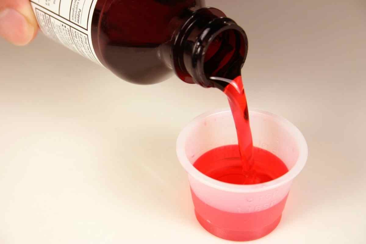 una mano versa una dose di sciroppo rosso