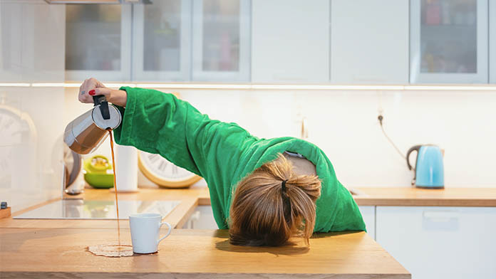 donna stanca per carenza di ferro che versa caffè fuori dalla tazza