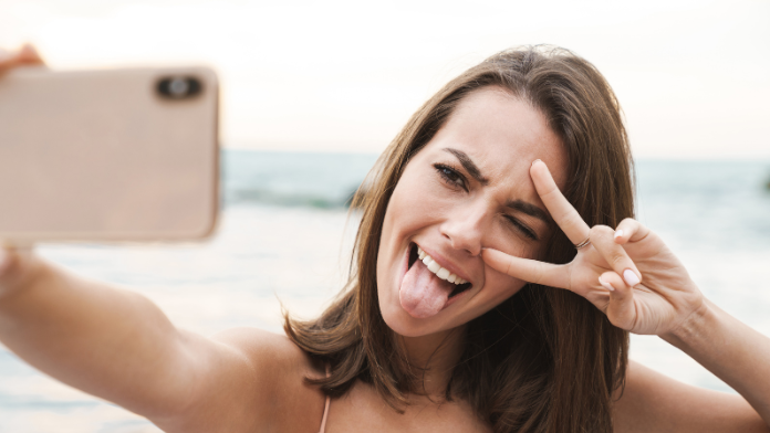 ragazza che si fa selfie al sole in spiaggia con linguaccia