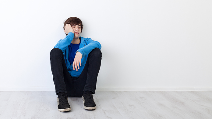 Un ragazzo è seduto a terra appoggiato a un muro con un atteggiamento apatico