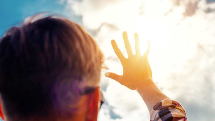 un uomo si ripara con una mano dai raggi del sole