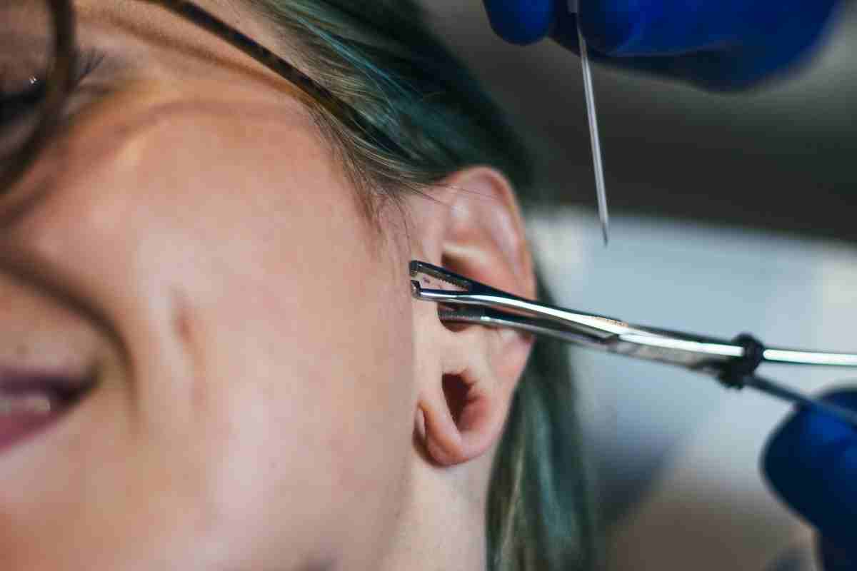 un piercer procede a fare un buco a un orecchio