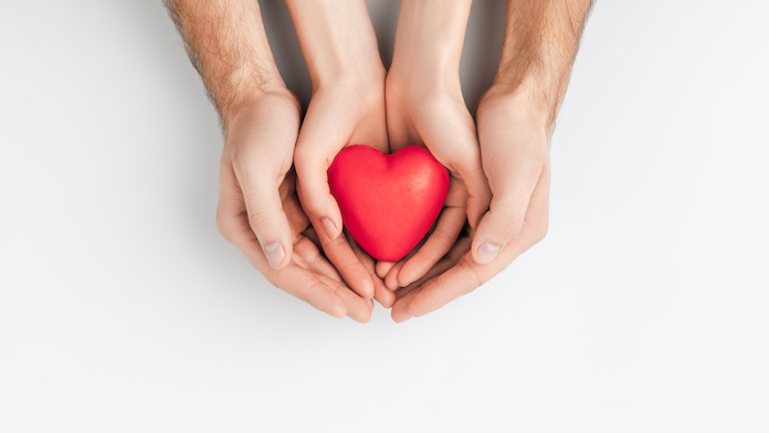 un papà stringe le mani di un bambino che ha un cuore in mano