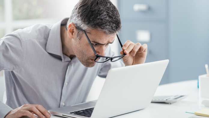 un uomo fa fatica a leggere la schermata del suo computer