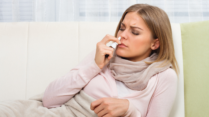 Una ragazza con raffreddore usa uno spray nasale per liberare il naso