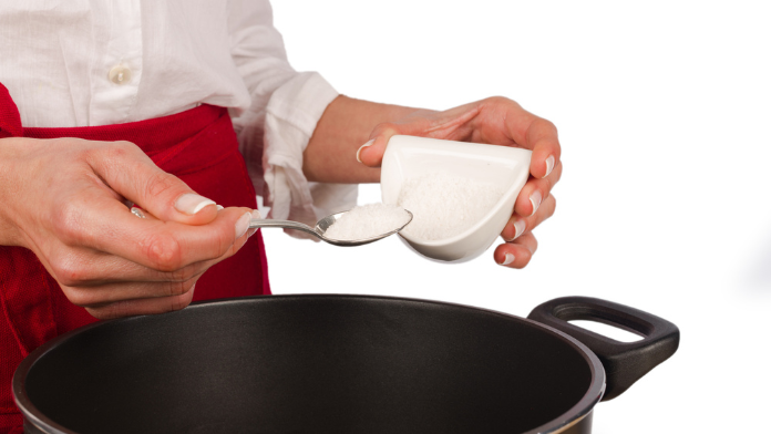 una cuoca versa un cucchiaio di sale in una pentola