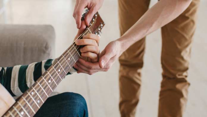 un musicista insegna a suonare la chitarra a un allievo