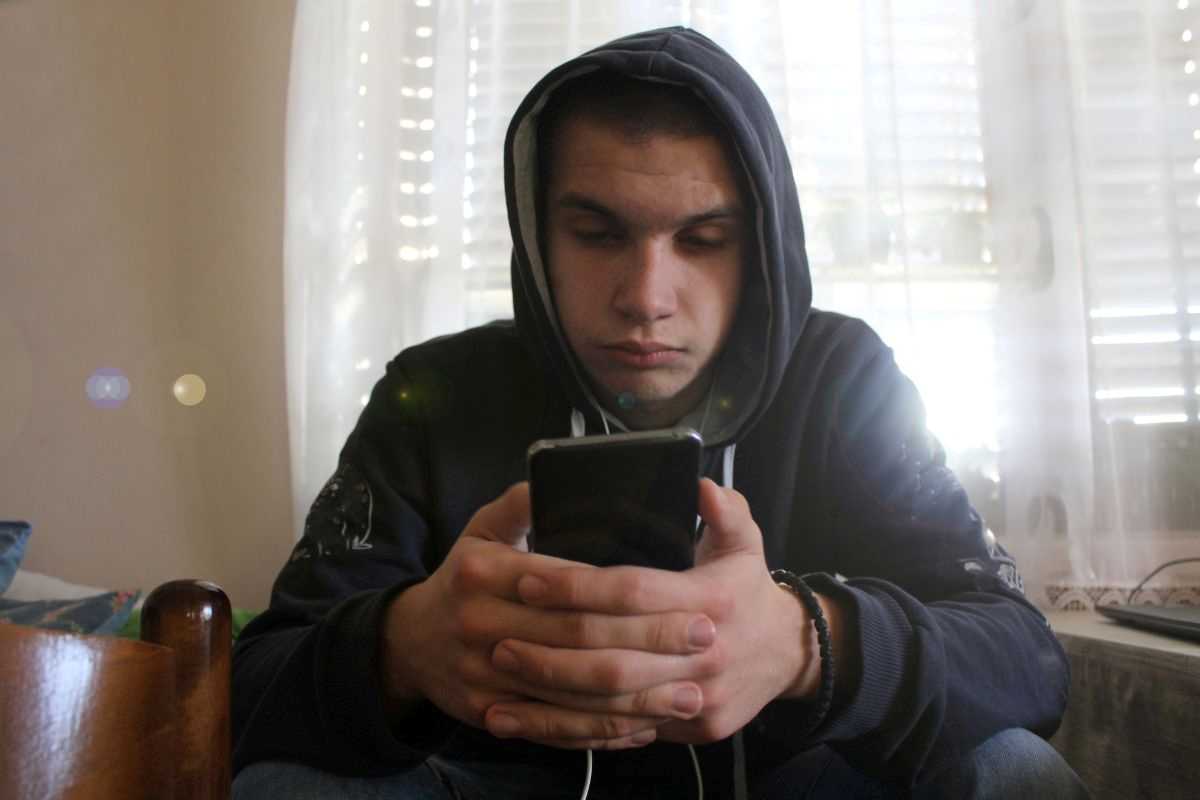 ragazzo con cappuccio sulla testa guarda il suo smartphone