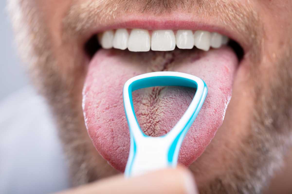 un uomo si pulisce la lingua con l'apposito strumento
