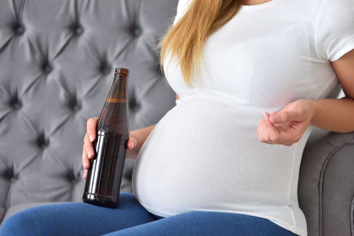 donna incinta che regge una bottiglia di birra in mano