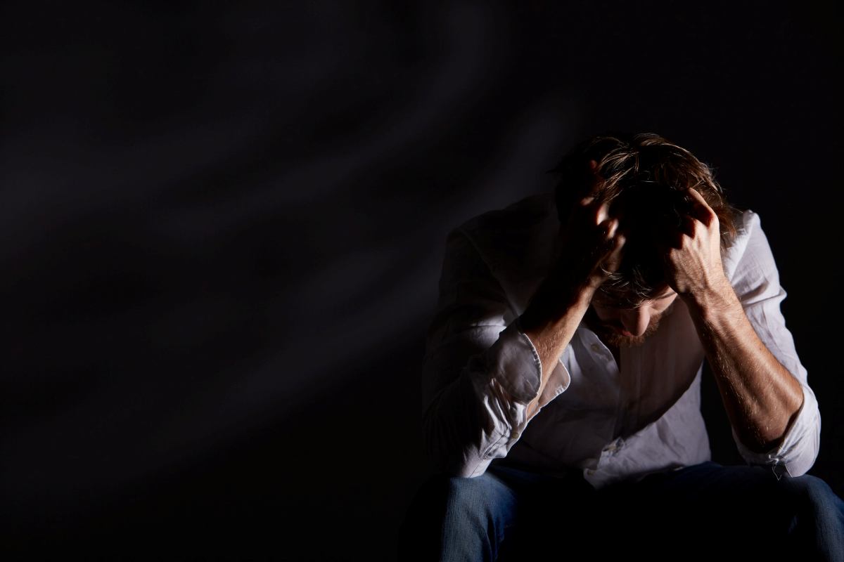 uomo al buio si porta le mani ai capelli per disperazione