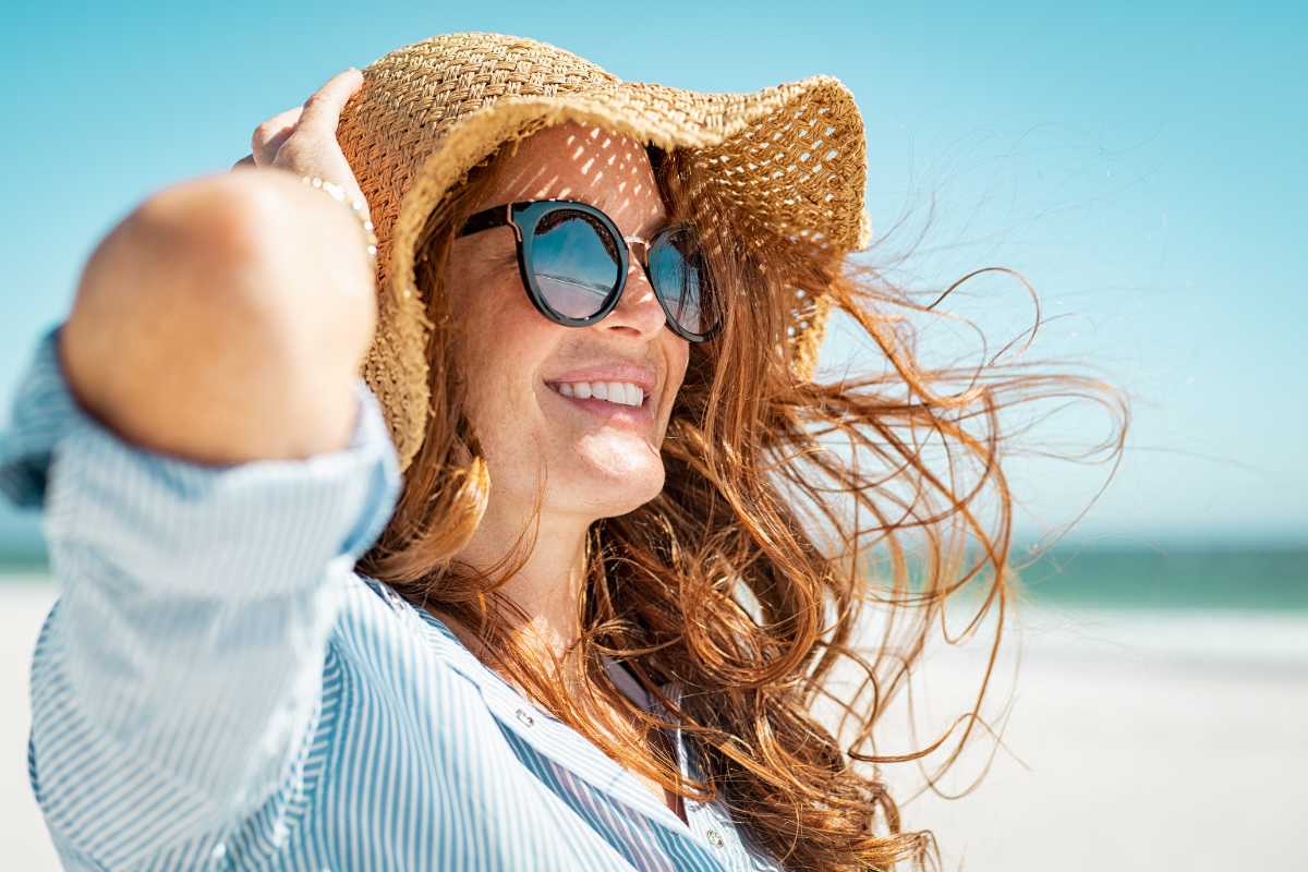 donna in spiaggia con cappello a tese larghe e occhiali da sole