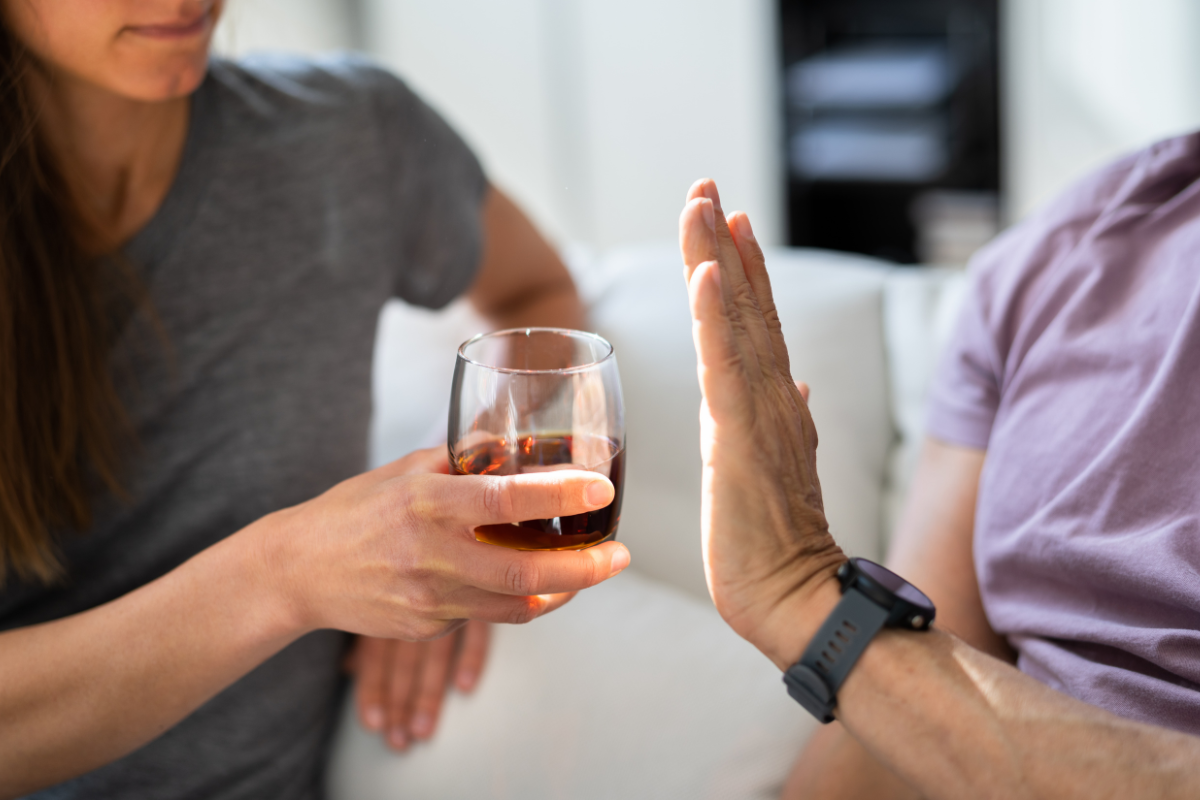 una donna offre un bicchiere di amaro a un uomo che rifiuta con il gesto della mano
