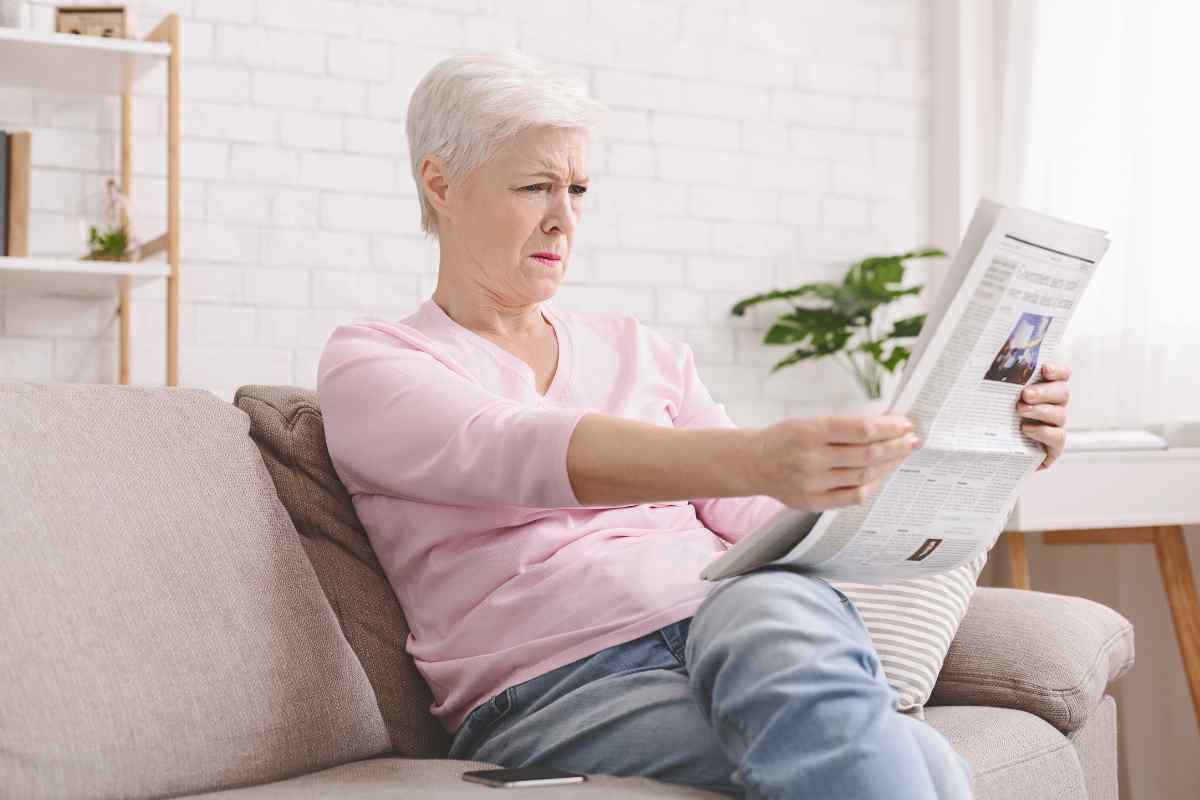 una donna allontana da sé il giornale perché non riesce a leggerlo