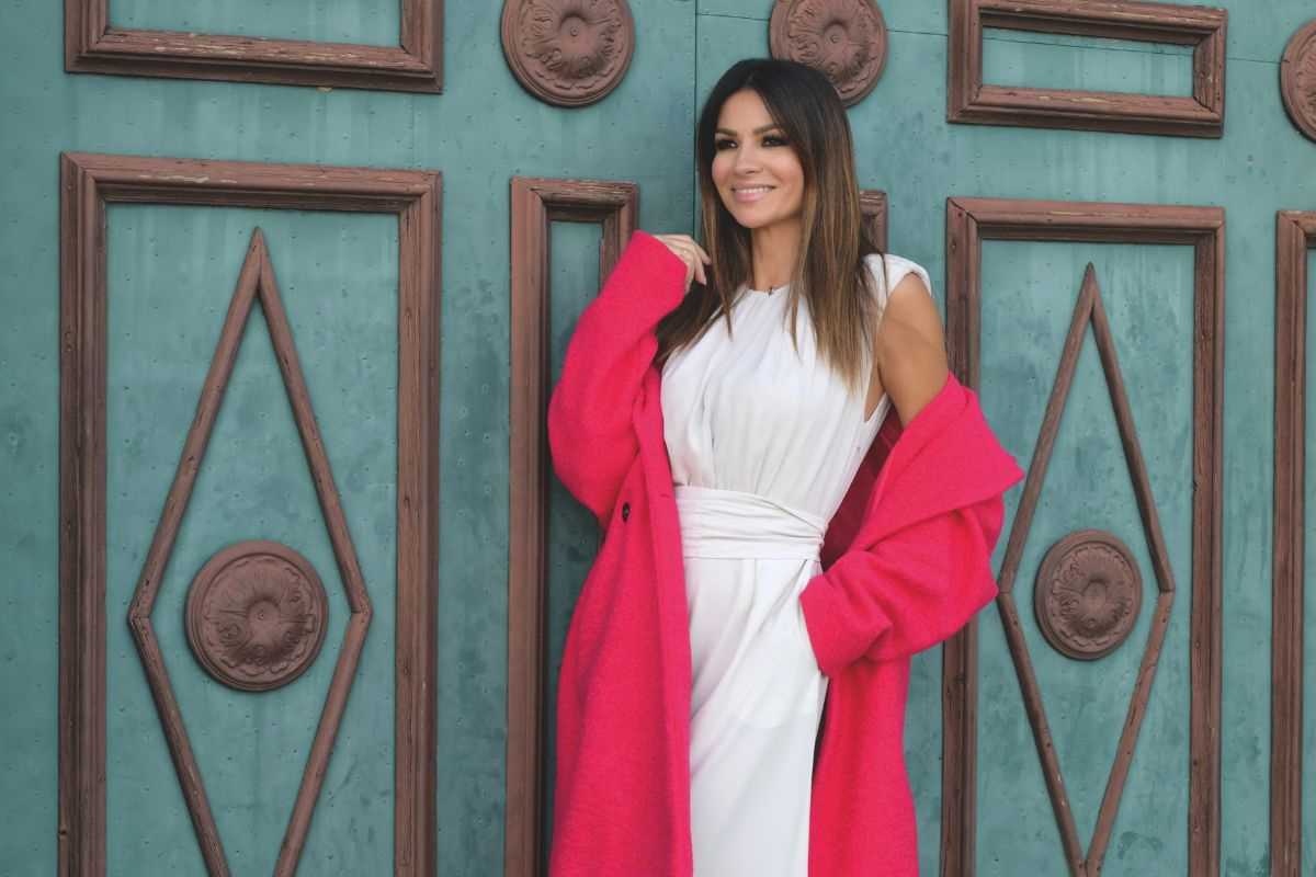 alessia ventura posa con abito bianco e soprabito fucsia appoggiata a una porta