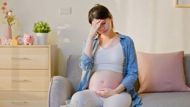 donna incinta seduta sul divano che si tiene il pancione con una mano; l'altra mano è appoggiata sulla fronte