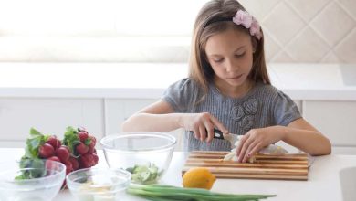 bambina che cucina, tagliando un alimento su un tagliere