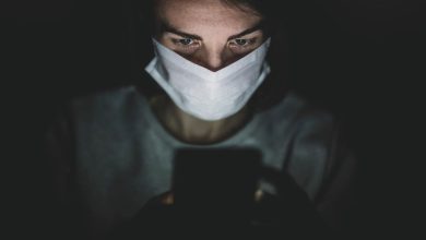 donna in penombra con indosso una mascherina chirurgica mentre guarda lo smartphone