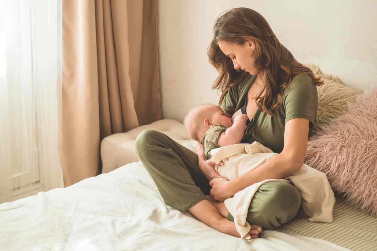 donna seduta sul letto che allatta il suo bambino