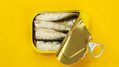 scatoletta semi-aperta di sardine in primo piano su sfondo giallo