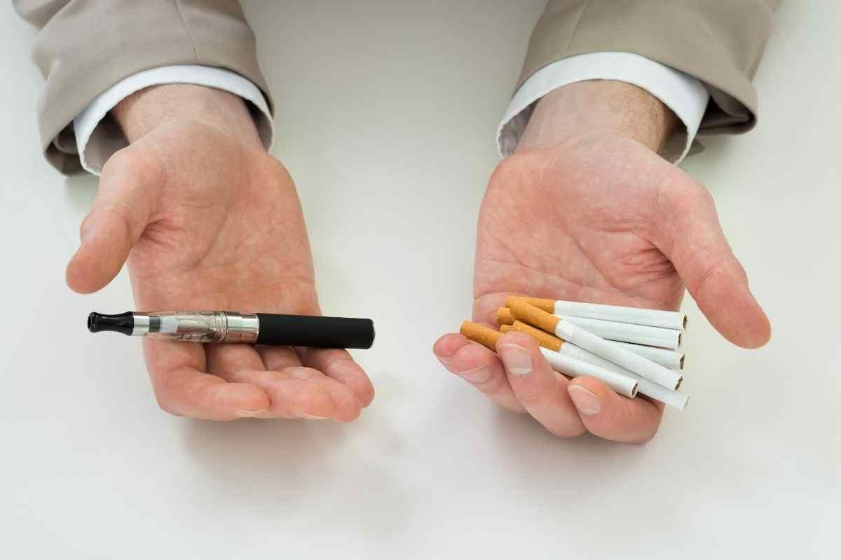un uomo ha sulla mano destra una sigaretta elettronica sulla sinistra delle sigarette tradizionali