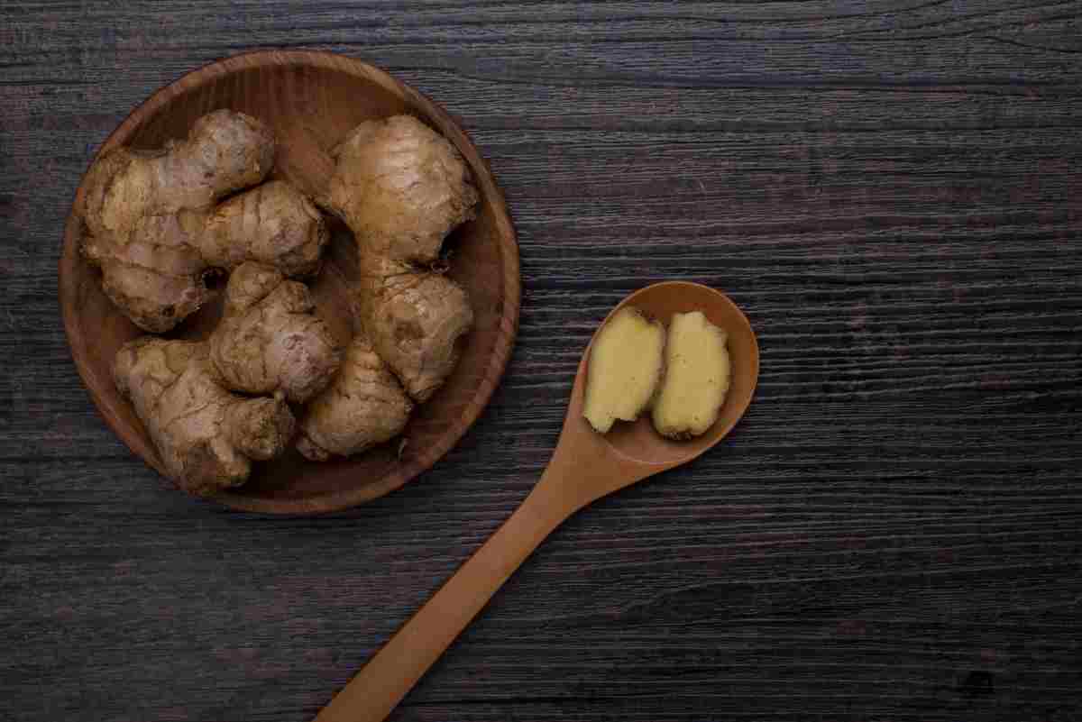 una ciotola con radici di zenzero e un cucchiaio che contiene zenzero fresco sbucciato