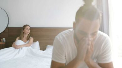 coppia a letto: la donna guarda fuori dalla finestra, mentre l'uomo si mette le mani sulla faccia preoccupato per il calo del desiderio sessuale femminile