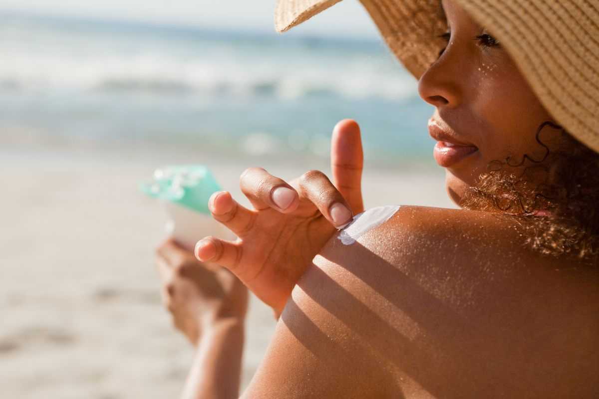 donna in spiaggia che si spalma la crema solare sulla spalla