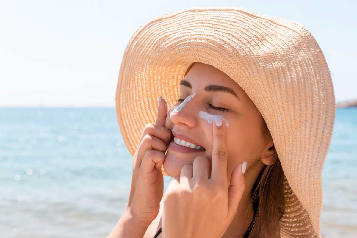 donna in spiaggia che si mette la crema solare sul viso