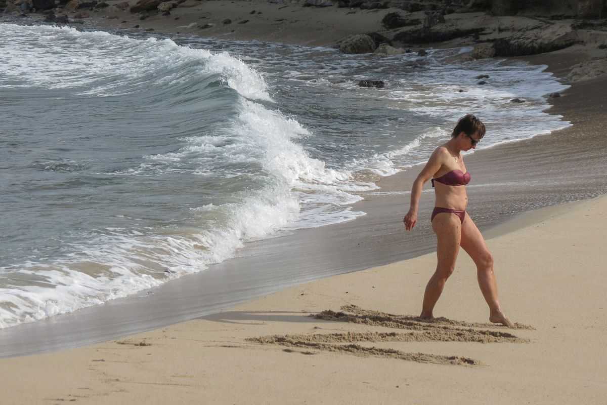 donna in riva al mare che scrive coi piedi sulla sabbia