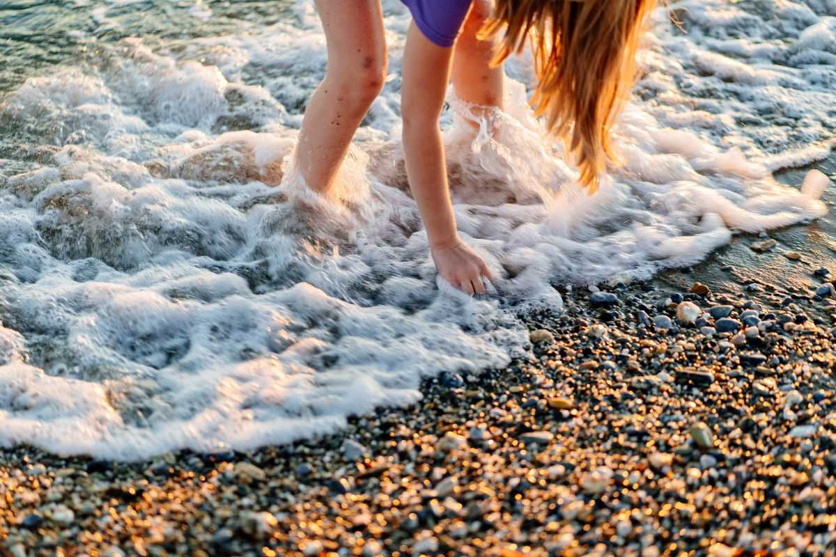 ragazza che raccoglie conchiglie in riva al mare e fa esercizi in spiaggia