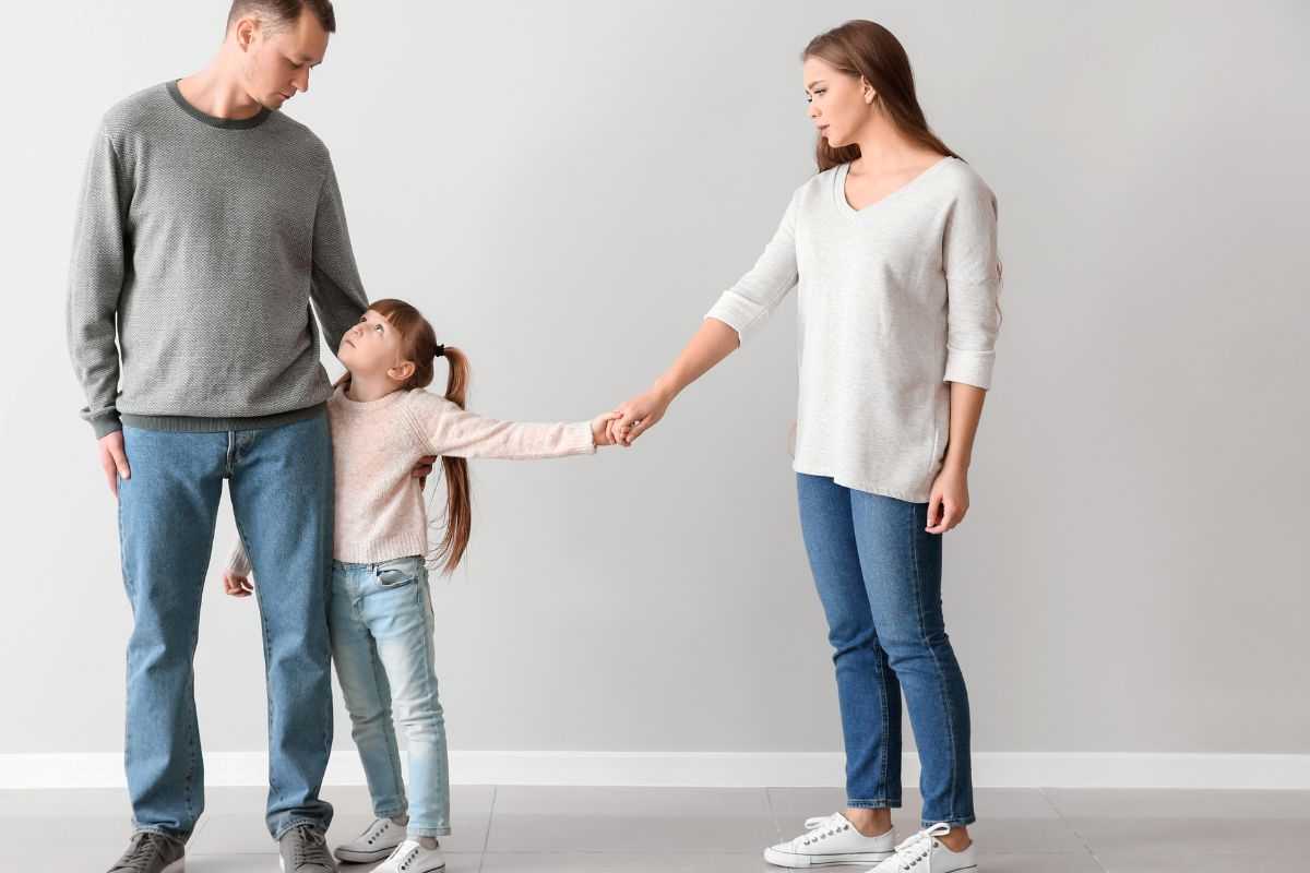 coppia di genitori separati con figlia che va ad abbracciare il padre mentre tiene la mano alla mamma