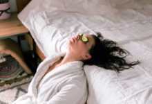donna in vacanza che indossa un accappatoio e si appoggia al letto con fette di cetrioli sugli occhi