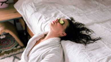 donna in vacanza che indossa un accappatoio e si appoggia al letto con fette di cetrioli sugli occhi