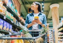 donna che fa la spesa al supermercato controllando la lista della spesa sul cellulare