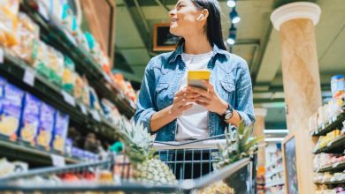 donna che fa la spesa al supermercato controllando la lista della spesa sul cellulare